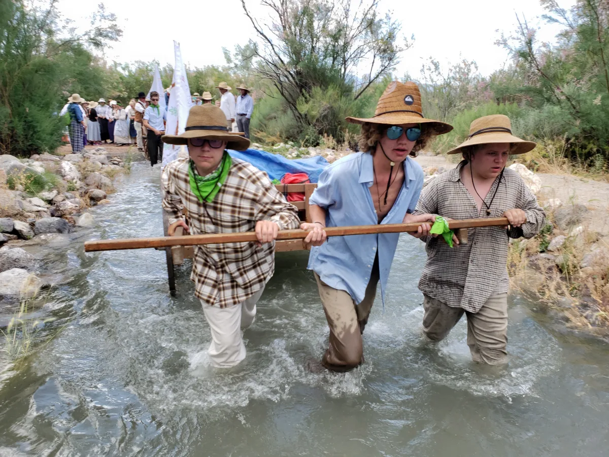 Young men in pioneer trek clothing: long-sleeved button-up shirts, suspenders, and wide-brim hats